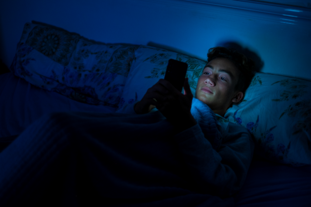 Jovem deitado com celular.